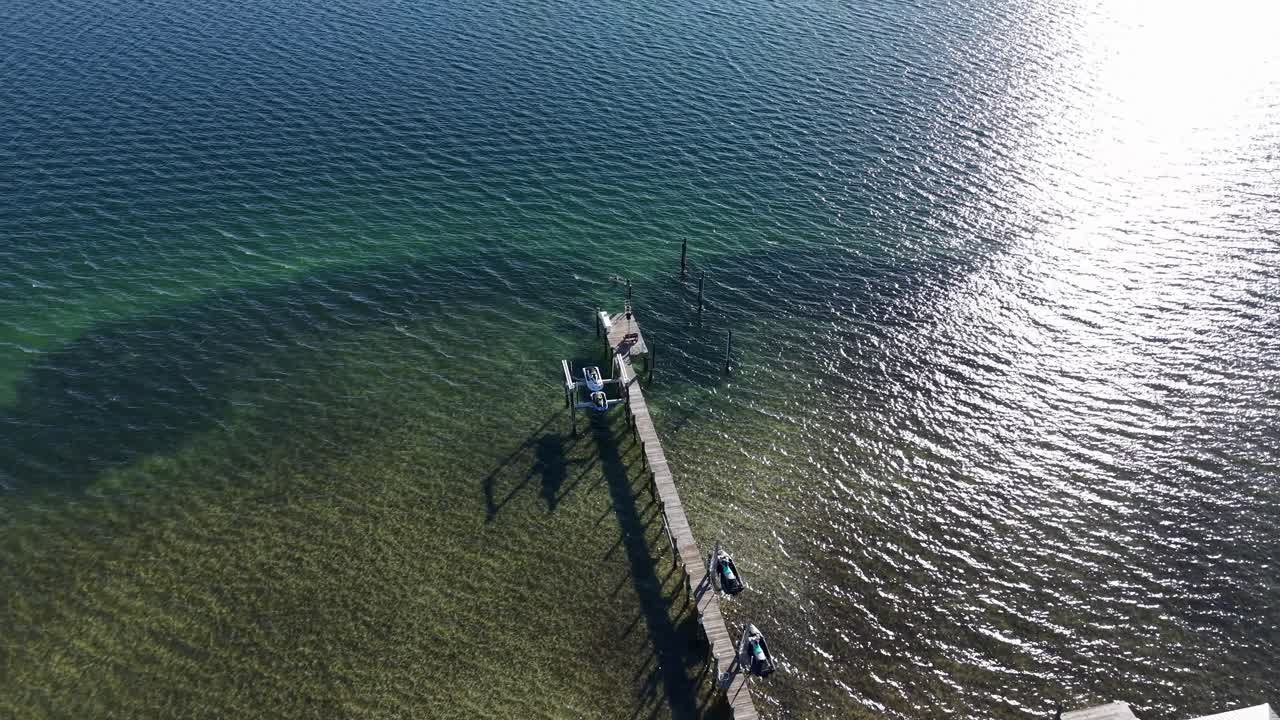 Dynamic drone fly from a pier to a sailboat gliding over calm green coastal bay water, Panama City Beach, Florida, USA