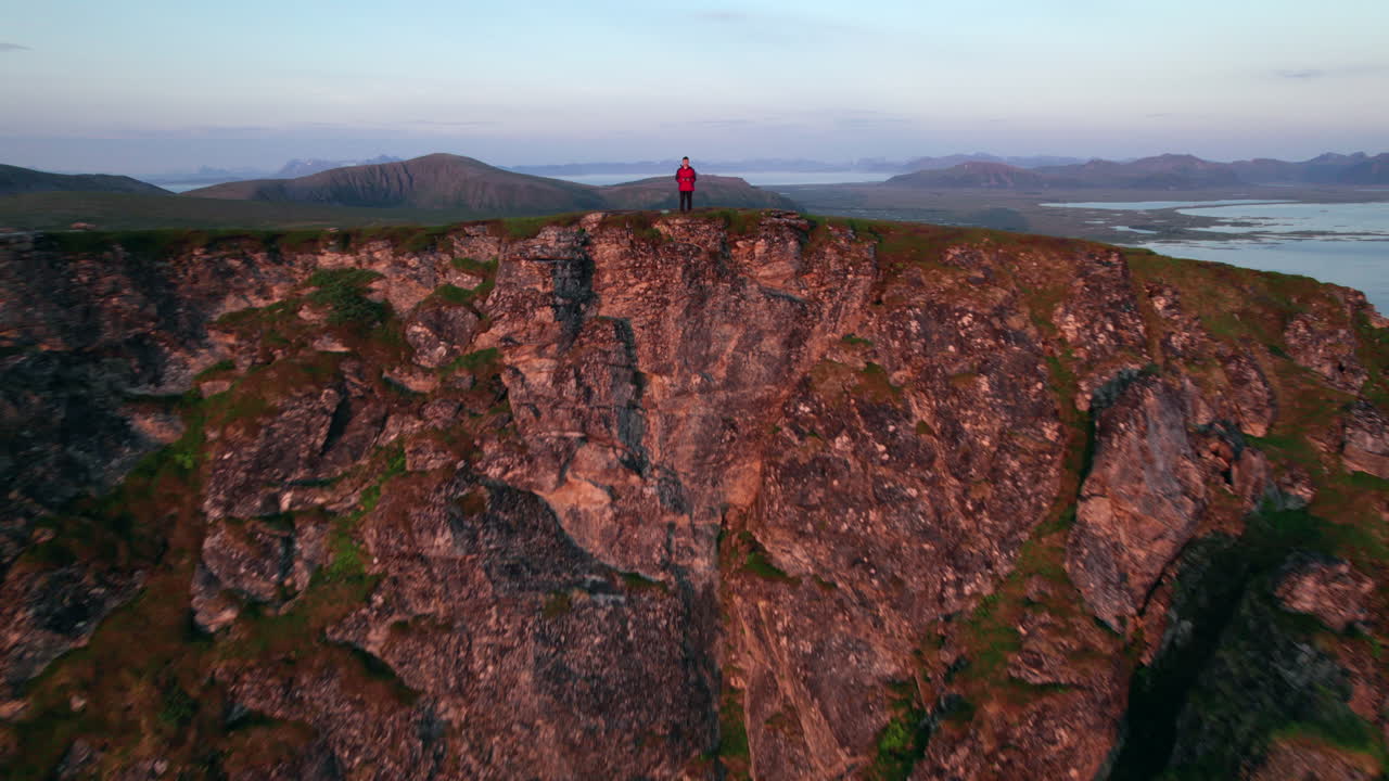 toma aérea de un hombre parado en la cima de una ola de montaña a la cámara antes de que retroceda para revelar un hermoso paisaje montañoso en la costa, matinden en andoya en noruega