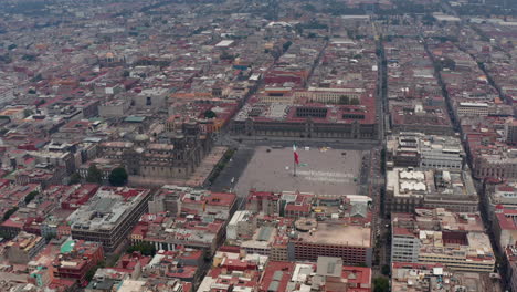 Forwards-Reveal-Of-Catedral-Metropolitana-De-La-Ciudad-De-Mexico-And-Plaza-De-La-Constitucion-With-Large-State-Flag.-Aerial-Footage-Of-Historic-City-Centre.-Mexico-City,-Mexico.