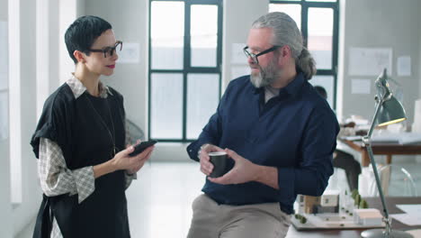 Dos-Colegas-De-Mediana-Edad-Conversando-Sobre-Un-Café-En-La-Oficina