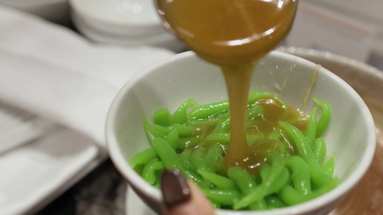 Close-up shot of brown coconut syrup poured over green pandan noodles in a bowl