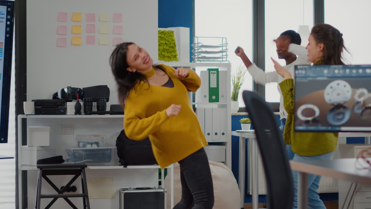Donne felici e diverse che ballano in un ufficio aziendale celebrando il successo di un progetto.