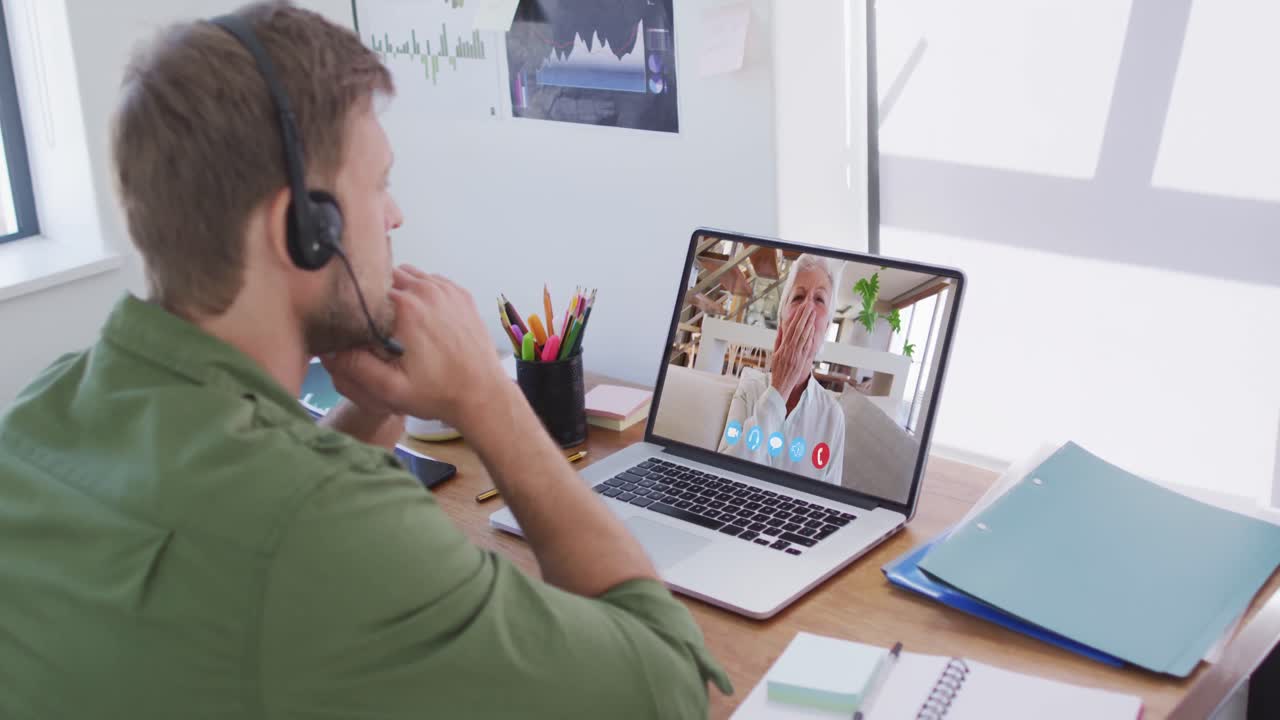Kaukasisk mand i en videochat på en bærbar computer, iført telefonheadset derhjemme.