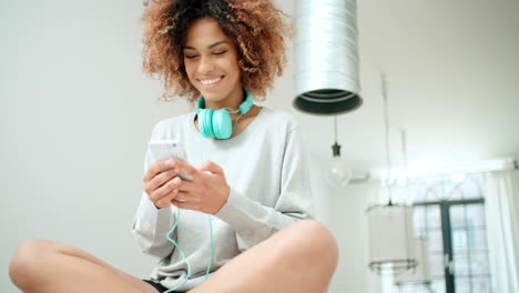 una hermosa joven afroamericana enviando mensajes de texto por teléfono móvil en casa.