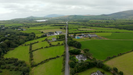 Backwards-fly-above-long-straight-road-leading-through-countryside.-Green-fields-and-pastures-divided-into-small-parts.-Ireland