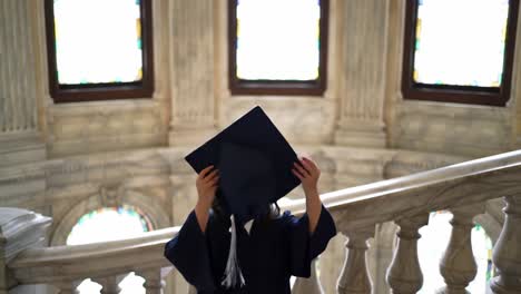 a joyful graduate throws her cap in the air while standing on a grand staircase. the elegant architecture and stained glass windows create a memorable backdrop for this special moment.