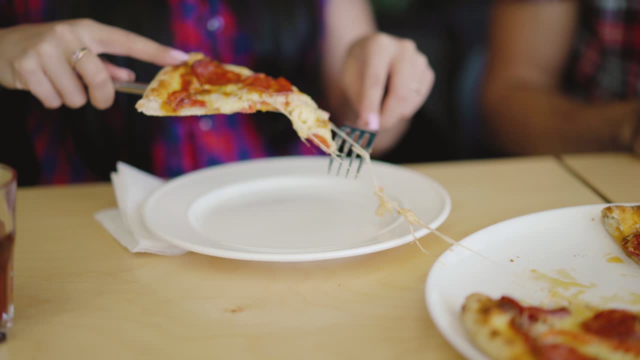 woman is cutting a piece of hot pizza and putting it in her plate at the table in the pizzeria. Blurred background