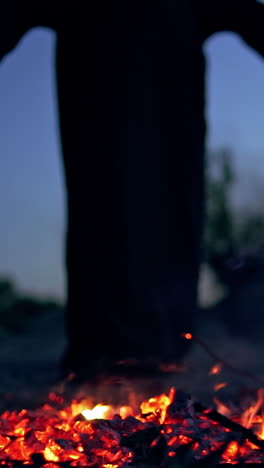 spooky death in black gown near fire. embers of fire on the ground and mysterious figure doing shamanism with a wooden stick. halloween day. vertical video