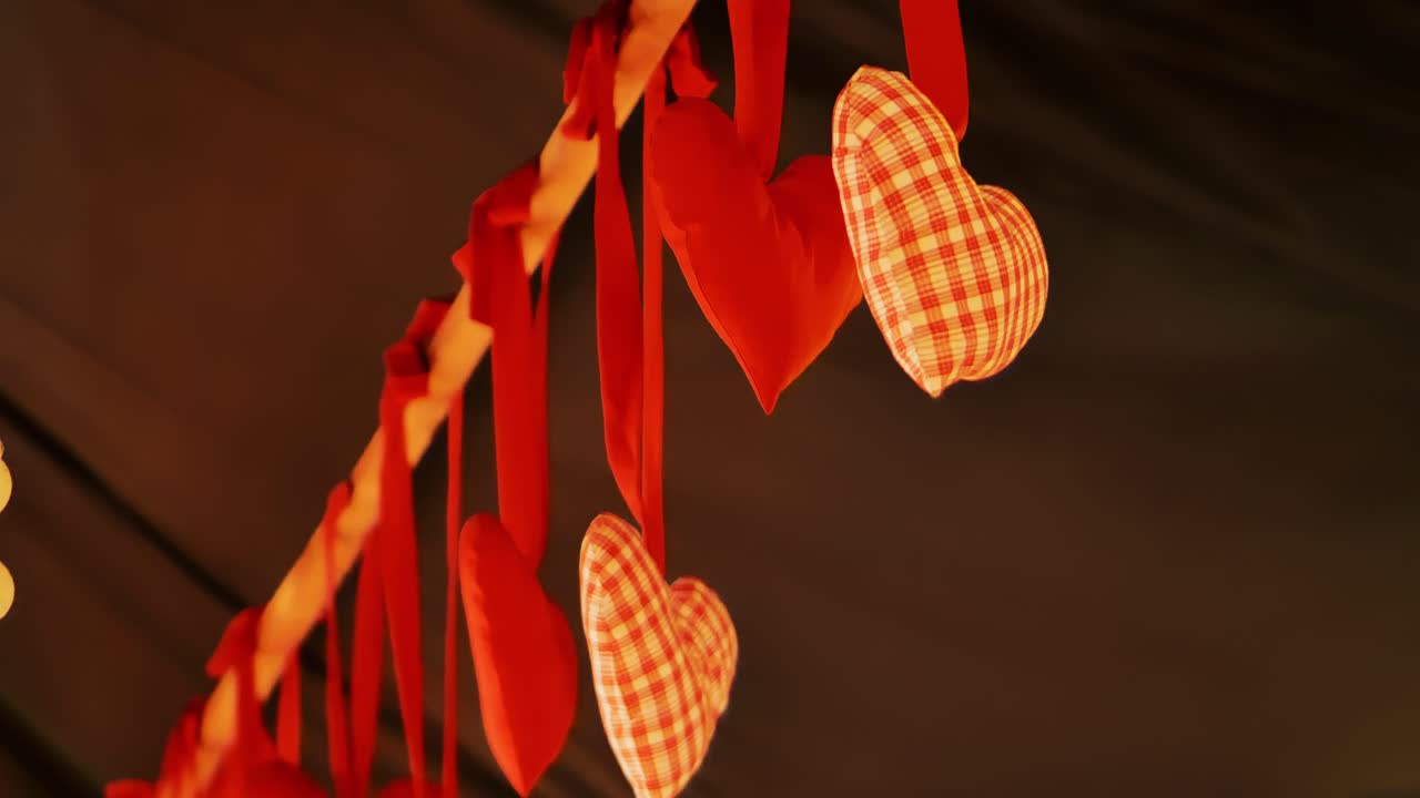Soft handmade hearts sway gently in festive Valentine setup under warm lights