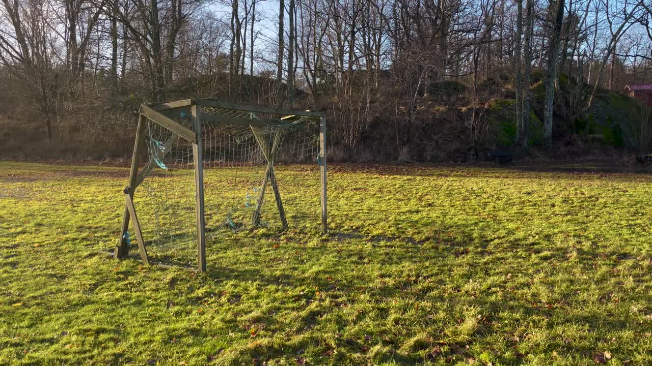 Old wooden soccer goal on empty grass field by forest at sunset