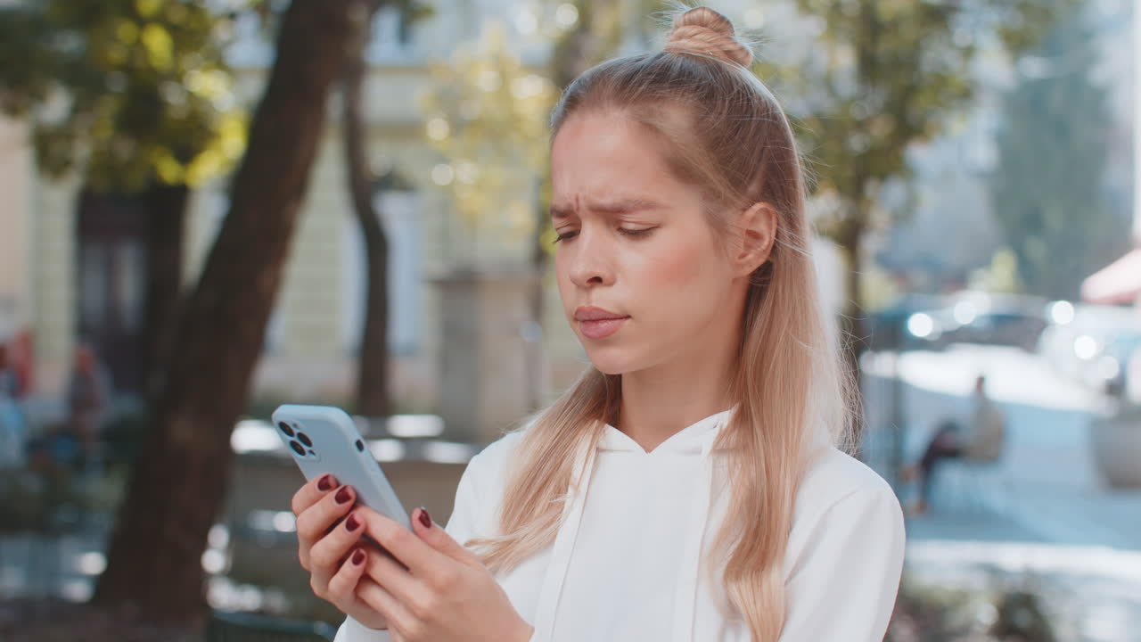 Young woman using cellphone typing browsing loses becoming shocked sudden lottery results on street