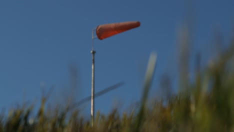 Abstract-red-wind-sock-blowing-horizontally-in-gale,-with-fast-moving-green-vegetation-in-foreground