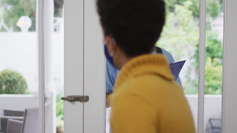 médico de raza mixta con máscara facial llamando a las puertas en casa