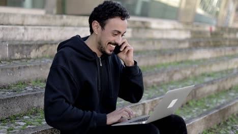 hombre alegre usando computadora portátil y teléfono inteligente