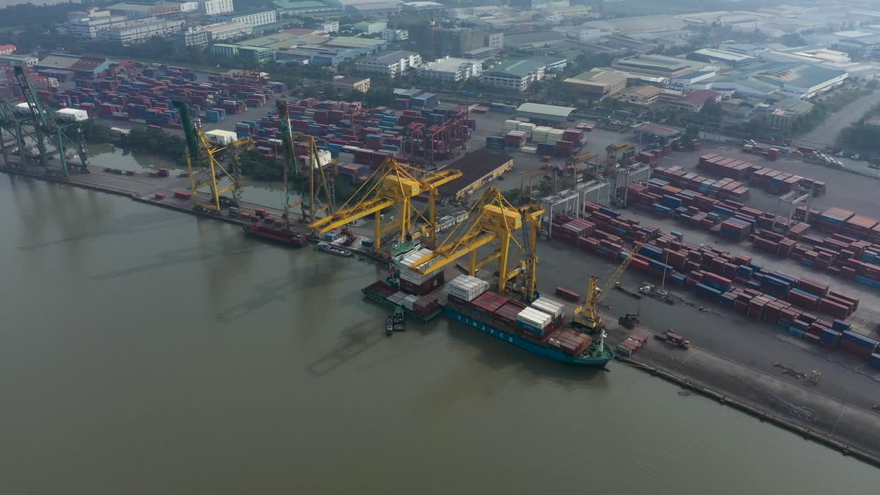 Drone flying in over Saigon river and port in Ho Chi Minh City, Vietnam with container ship and large working cranes