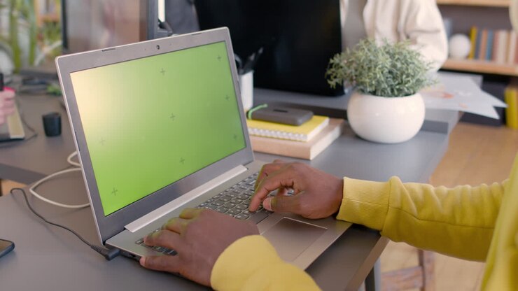 Gros plan sur un homme méconnaissable travaillant sur un ordinateur portable moderne avec écran vert au bureau