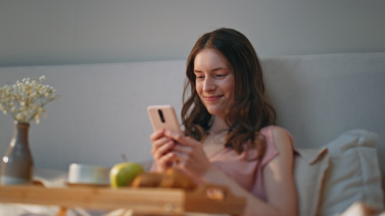 chica soñadora escribiendo teléfono móvil en casa de cerca. modelo sonriente acostado en una cama acogedora