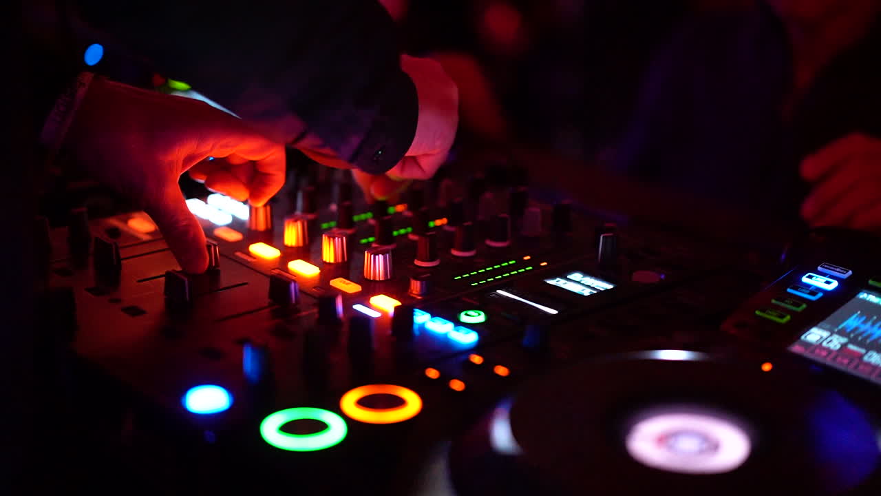 The DJ at his mixer table at the nightclub turning the knobs and pushing buttons with flashing lights