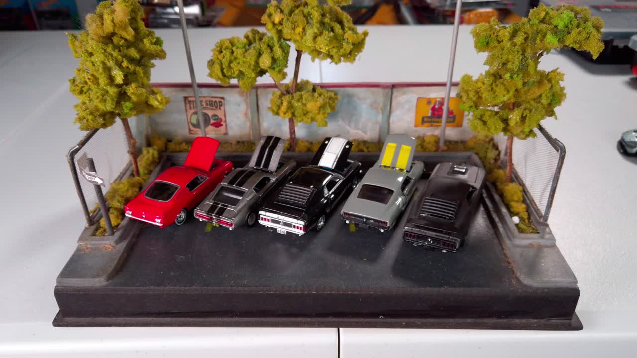 Zoom out from a close-up of parked toy muscle cars in a detailed miniature garage scene. Creative diorama with handcrafted trees.