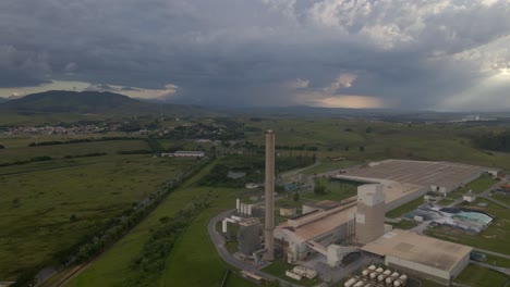 Luftaufnahme-Einer-Mittelgroßen-Fabrik-Mit-Dramatischem-Himmel-Und-Umgebendem-Grün