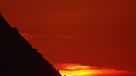 the sun sets behind a mountain with a glowing orange sky creating a dramatic scene