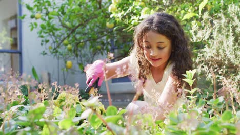 Hija-De-Raza-Mixta-Jardinería-En-Un-Jardín-Soleado,-Cuidando-Las-Plantas