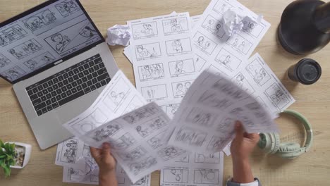 close up top view of male artist's hands holding sketching papers, choosing, then throwing on the table with a laptop and headphones in the studio