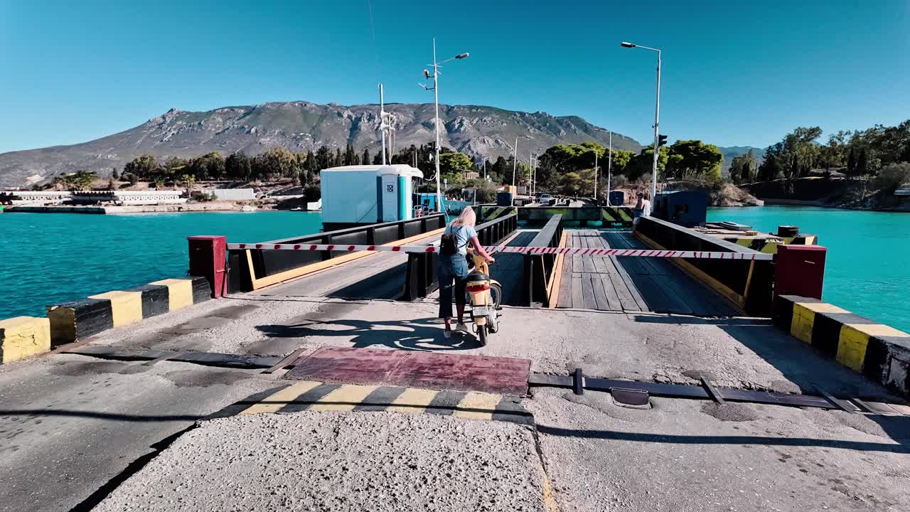 Woman on a scooter crossing a bridge over water with mountains in the background