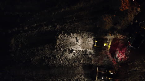 Bulldozers-work-at-night-at-snow-depot-after-blizzard,-rising-aerial