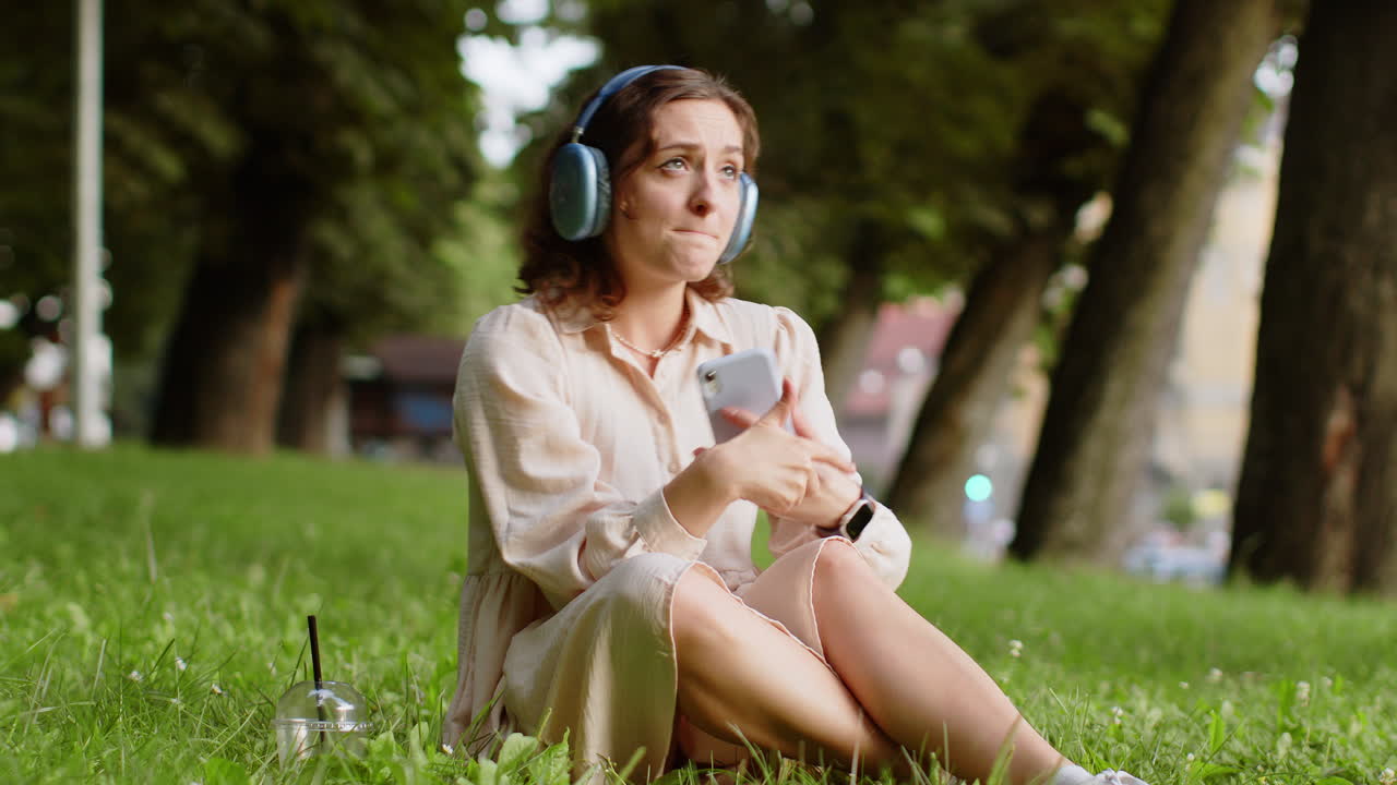 Happy young woman in wireless headphones choosing listening music in smartphone dancing outdoors