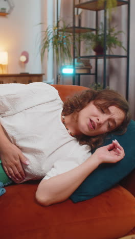 sick ill young woman lady suffering from period cramps painful stomach ache on sofa couch at home