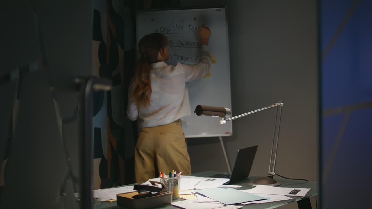 Overworked lady writing whiteboard at evening cabinet. Woman working late office