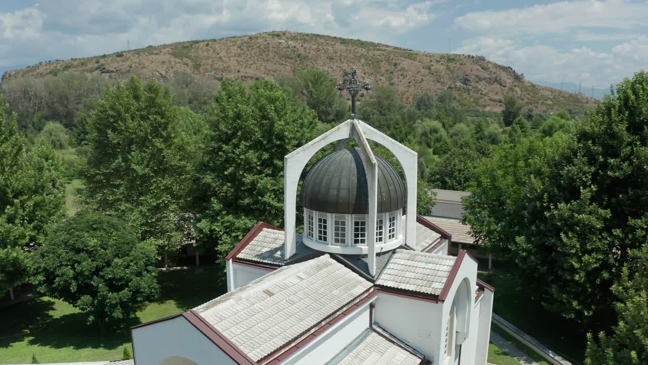 Pedestal drone shot of St Petka Church's dome, and slowly orbitting around the rest of the buildings around the church, revealing the surrounding trees and mountains