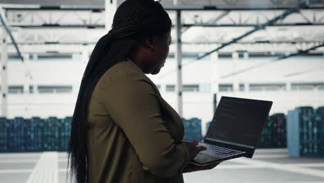 technician with laptop walks through data center server rows