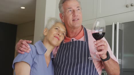 Feliz-Pareja-De-Ancianos-Caucásicos-Usando-Delantales-Abrazándose-Y-Bebiendo-Vino