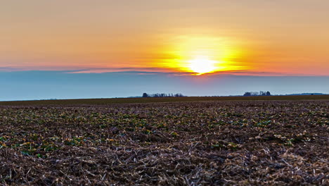 tiro de lapso de tiempo de la puesta de sol dorada detrás de las nubes sobre el campo agrícola, plano general