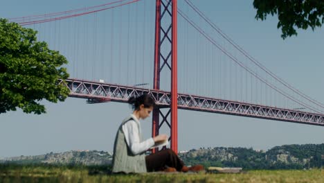 woman reading in a park underneath the bridge of the 25th of april