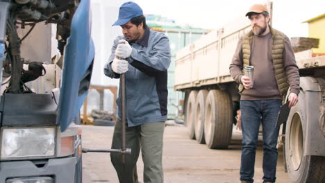 worker fixing a truck in a logistics park while being supervised by his boss 1