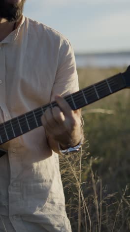 man playing electric guitar in a field at golden hour