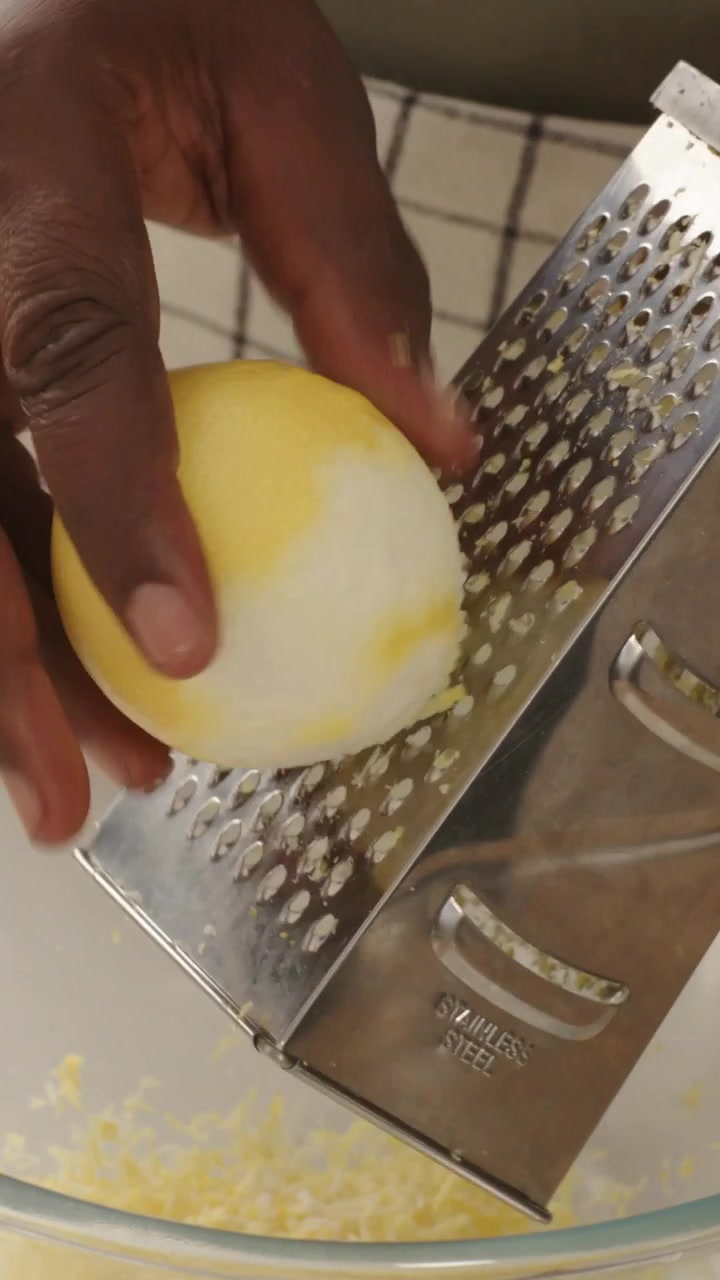 Video verticale: Uomo con maglietta color kaki mette un limone sbucciato sulla grattugia e grattugia la scorza in una ciotola per una ricetta.