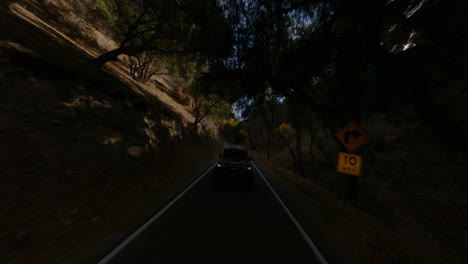 fpv drone shot of black car driving fast on tiny road