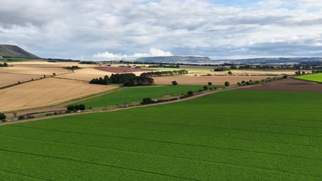 aerial camera smoothly pans across lush green and golden farmland under partly cloudy skies, revealing rolling countryside and distant hills in natural daylight