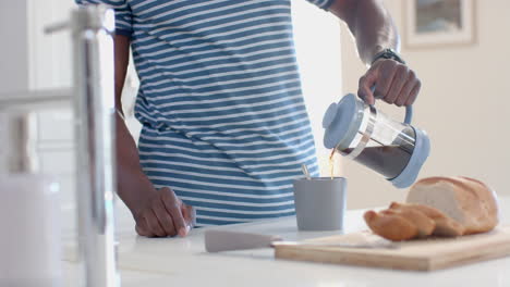 hombre afroamericano vertiendo café en una taza en una cocina soleada, en cámara lenta