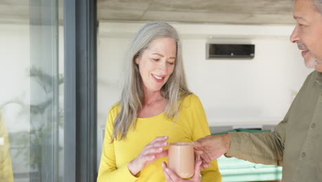smiling multiracial senior couple enjoying coffee together at home, spending quality time