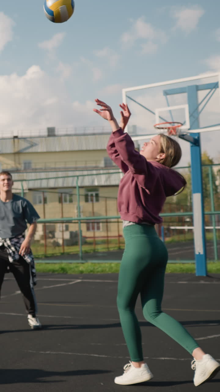 instructor conduce sesión de entrenamiento de voleibol con tres damas pasando la pelota en la cancha al aire libre, mostrando trabajo en equipo y práctica, la escena incluye fondo con edificio, valla y cancha de baloncesto