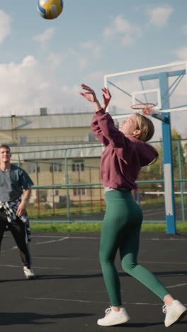 instructor conduce sesión de entrenamiento de voleibol con tres damas pasando la pelota en la cancha al aire libre, mostrando trabajo en equipo y práctica, la escena incluye fondo con edificio, valla y cancha de baloncesto