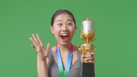 close up of asian woman with a gold medal looking at a gold trophy in her hands and saying wow being happy winning as the first winner on green screen background in the studio