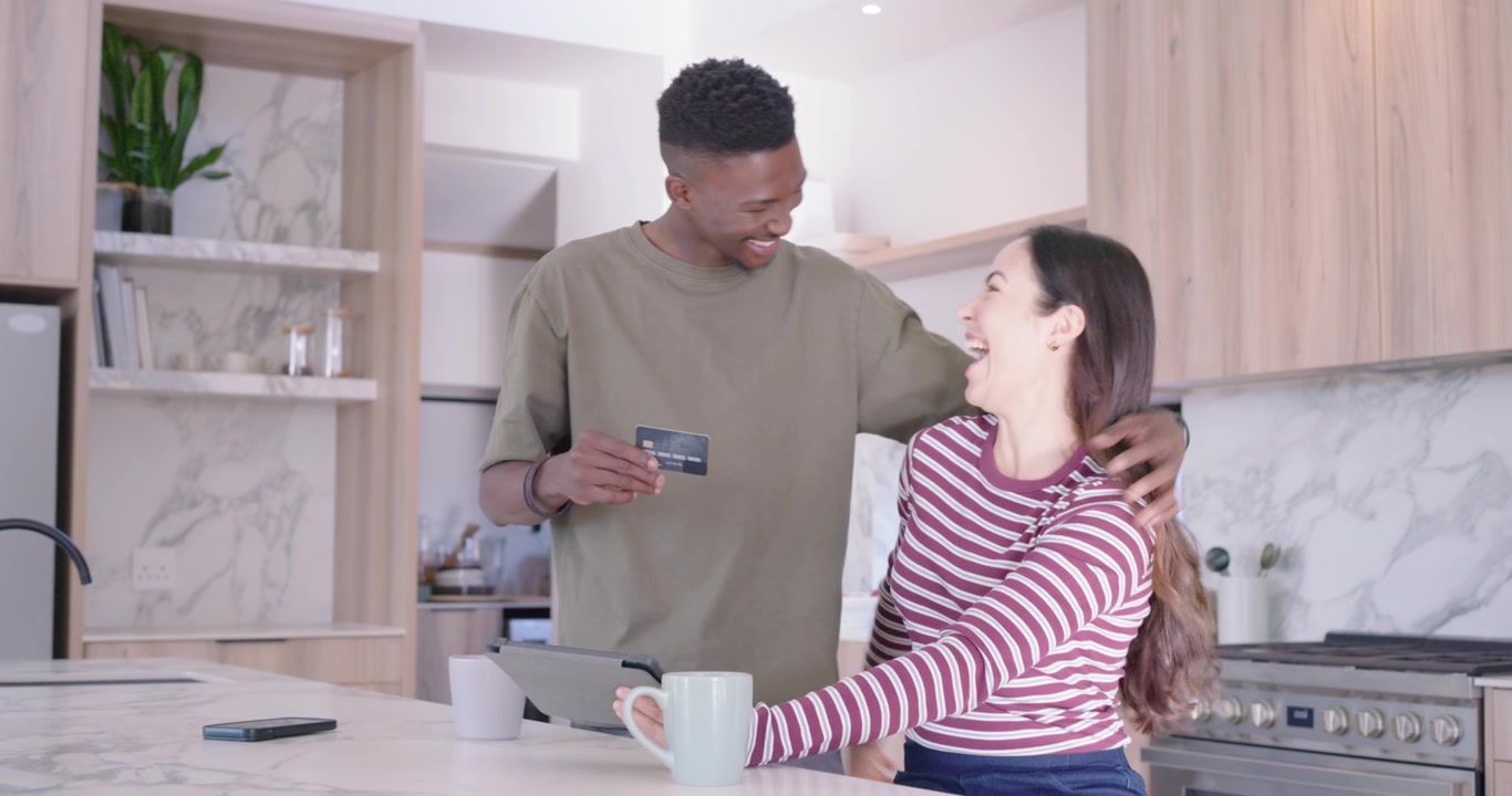 Couple sitting at kitchen island, woman tapping tablet after man holding card, finishing checkout