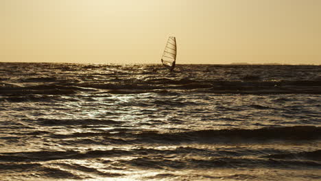 Einsamer-Windsurfer,-Der-Bei-Sonnenuntergang-Auf-Einem-Brett-Mit-Einem-Segel-Schwimmt