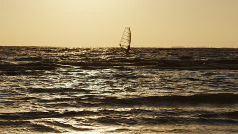 lone windsurfer floating on a board with a sail at sunset